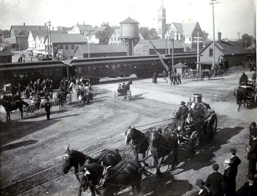 Black and White photograph of a horse drawn steamer and hose wagon going down old main street
